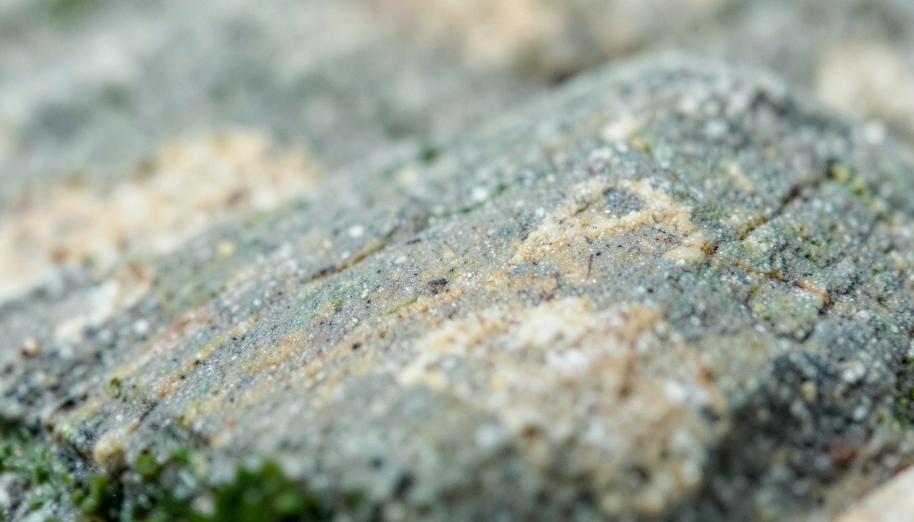 A close-up photograph of smooth, unpolished natural stone in muted greys and warm beige tones, with subtle veins and a soft matte texture